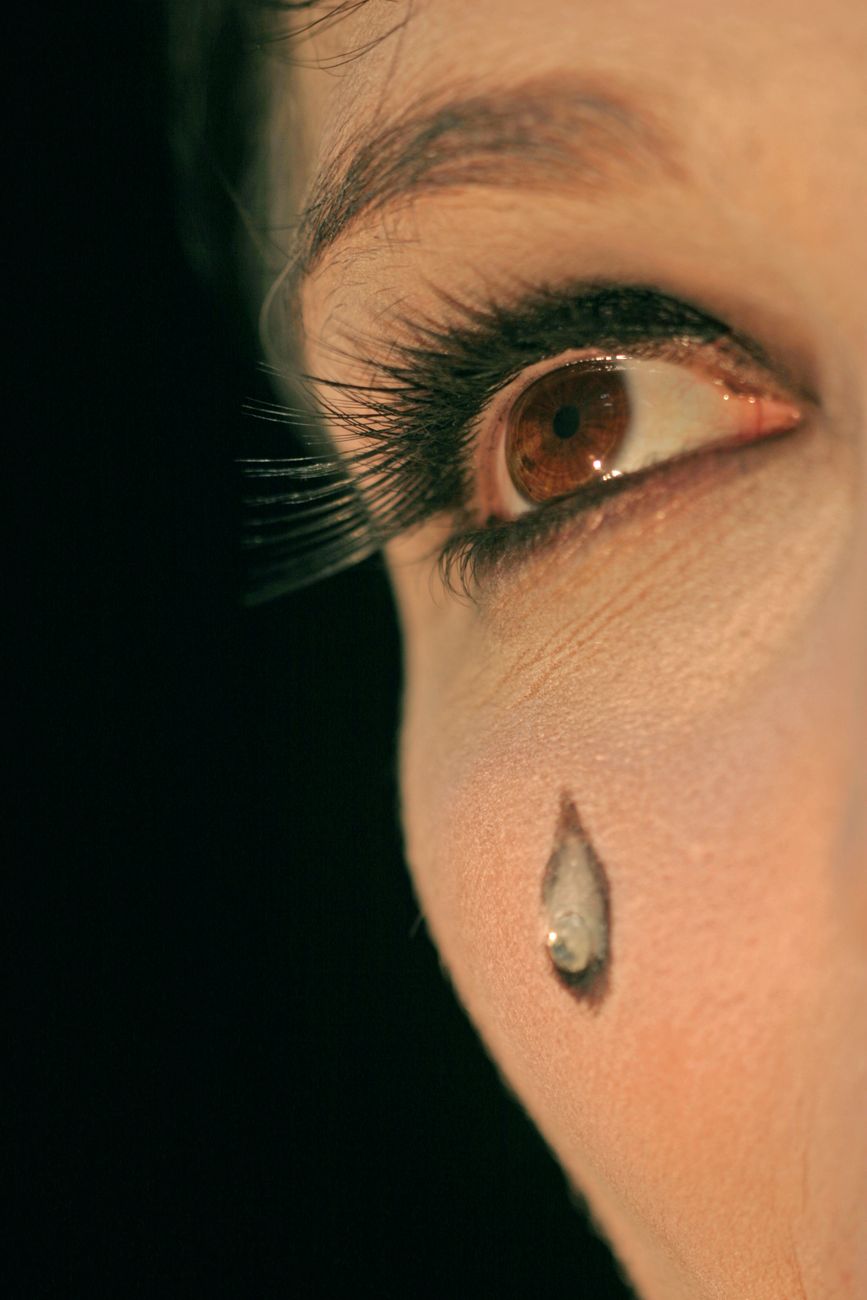Close-up of a woman's eye with long eyelashes, featuring a tear drop makeup design on her cheek.