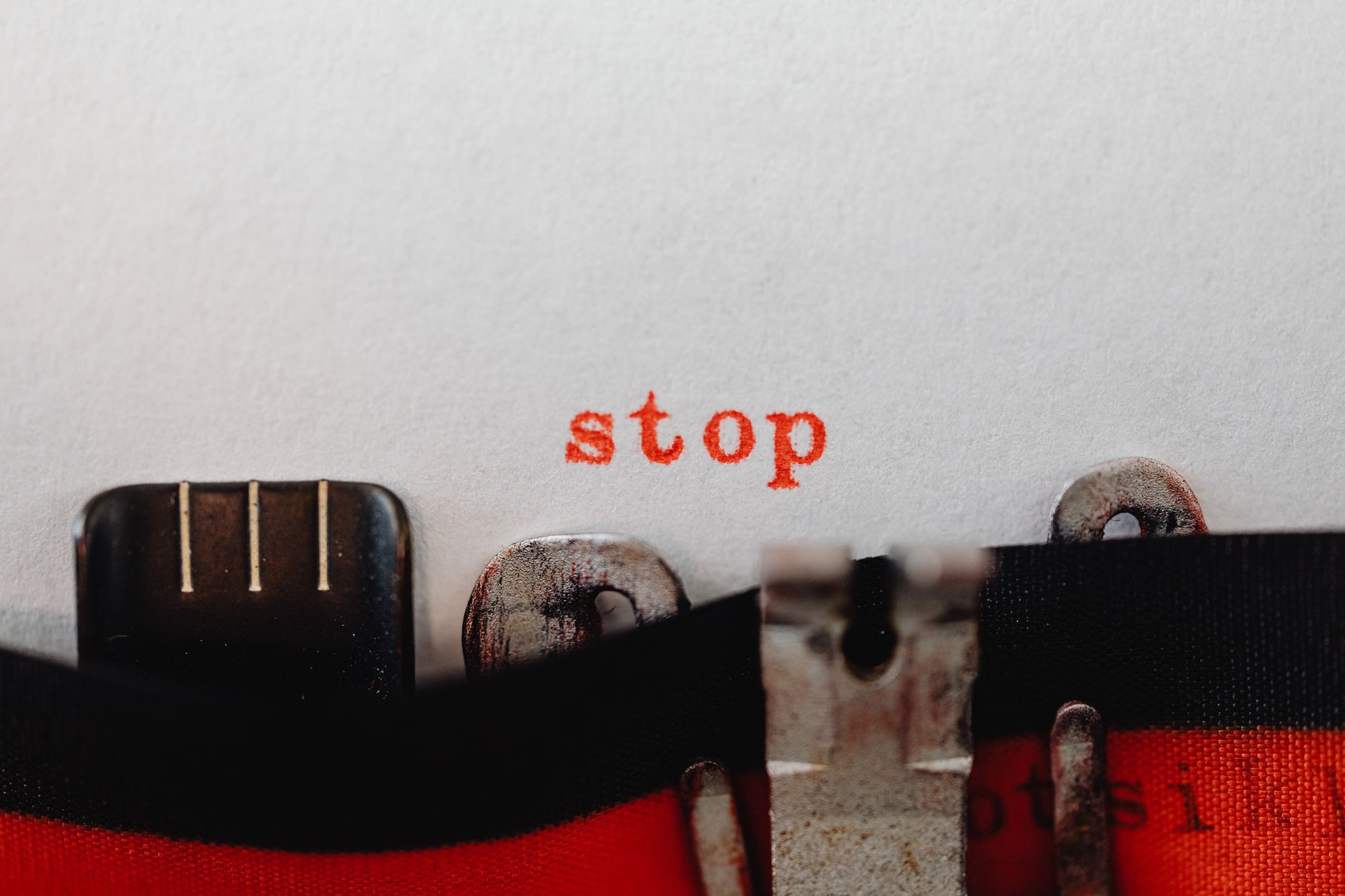 Close-up of a typewriter with the word 'stop' typed in orange ink on white paper.